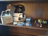 Shelf view showing Baofeng box with accessories, ProCase ear defenders, flashlights, battery packs