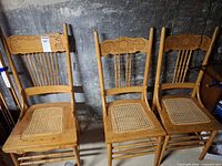 Front view of three pressed back chairs showing carving and cane seats