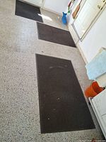 Three dark gray door mats laid out on speckled garage floor