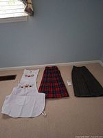 Group view of two embroidered white garments and two plaid skirts on floor