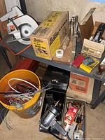 Overall lot on shelves showing circular saw, boxed mitre box, metal planes, bucket of wire, drill in tray