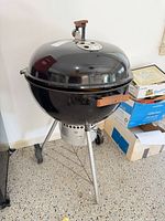 Full view of black Weber kettle grill on tripod stand with ash catcher