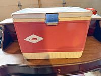Front view of red Coleman metal cooler on wooden surface