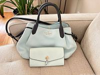 Satchel front view with wallet placed in front showing color, handles, strap, hardware