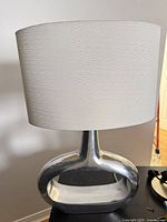 Front view showing silver metal base and white fabric shade