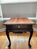 Front view of solid wood end table showing cabriole legs and brass drawer pull