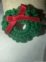 Front view of crocheted green wreath brooch with red ribbon bow