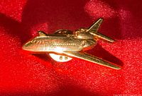Front view of gold-tone airplane brooch pin on red background