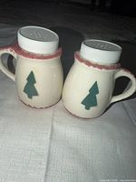 Front view of both ceramic shakers displaying tree motif and handles