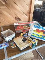 Overall lot on table showing Woodburning Set, Roller Coaster game, Perquackey, Orbeez jar, puzzle, wooden pieces box, model kit