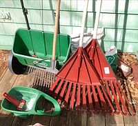 Two Scotts spreaders, three red leaf rakes, one metal bow rake, one ice scraper grouped on deck