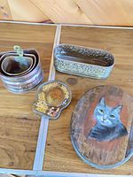 Group shot of all items: three nested copper planters, oval metal planter, resin seed trivet, wooden cat plaque