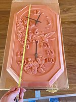 Front view showing clock, thermometer, relief design and measuring tape indicating size