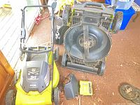 Two Ryobi cordless mowers underside view and charger