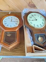 Two wooden pendulum wall clocks side by side