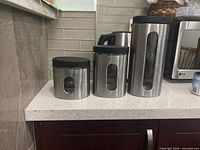 Front view of three stainless steel canisters showing glass windows