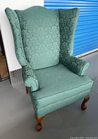 Front view of green damask wingback chair showing upholstery, arms, and cabriole legs