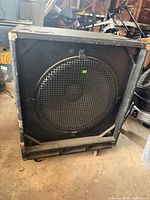Front view of speaker cabinet showing grille, casters, exterior wear