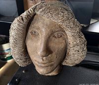 Front view of brown female head sculpture showing facial features and hair texture