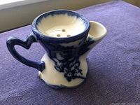 Front angle of blue and white ceramic shaving scuttle showing handle, floral motif, soap bowl and reservoir