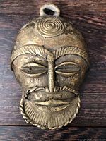 Front view of metal shaman mask showing facial features and hanging loop