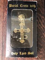 Front view of sealed box showing cross pendant and text