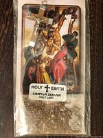 Front view of sealed package showing crucifix, prayer card and soil