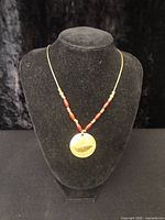 Front view of necklace on display bust showing brass pendant and red bead accents