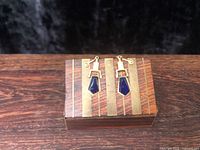 Earrings resting on striped hardwood box, front view