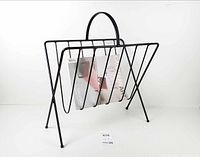 front view of black wrought iron magazine rack holding magazine for scale