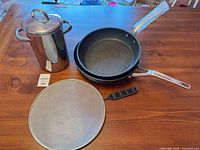 All cookware items: two The Rock frying pans stacked, stainless stockpot with lid, mesh splatter screen