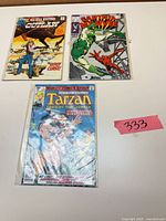 Three bagged comic books laid out: All-Star Western #10, Captain Marvel #12, Tarzan #1