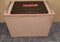 Front view of closed beige wicker storage box with black lid and metal handles