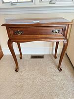 Front view of solid wood side table showing drawer with brass-tone hardware and cabriole legs