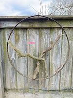 Full view of circular metal ring with branches hanging on wooden fence