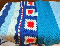 All three crocheted afghans folded side-by-side showing patterns and colors