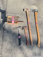 All tools laid out on pavement: two long axes, hatchet, hammer, chisels