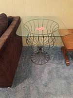 Side table positioned next to sofa and wooden table, showing full view of glass top and metal base