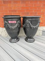 Front view of both black urn planters showing garland detail