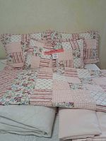 Quilt folded over foot of bed with pillow shams, decorative pillow, sheets and mattress pad visible