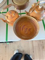 Overhead view showing two copper kettles and interior of copper bowl, portions of saucepan visible