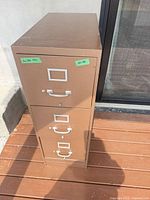 Front view of brown/tan 3-drawer metal filing cabinet with handles and label frames