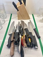 Pile of assorted knives on countertop with block behind