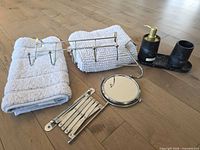 Full set showing two folded white bath mats, chrome five-hook rack, single hook, folded accordion mirror, soap dispenser, tumbler on tray