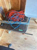 Top view of table saw showing metal tabletop, rip fence bar, coiled extension cords