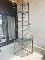 Full view of tall corner metal etagere showing four shelves and scrollwork frame