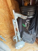 Collapsible grey golf cart beside Callaway bag
