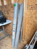 Two gray rolled ground covers leaning against plywood wall