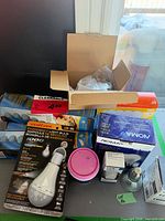 Overview of boxed bulbs, open carton with loose bulbs, NOMA packs, DryDex tub, loose reflector bulb