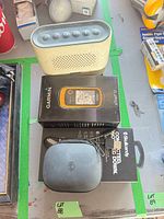 Top-down view of Bose speaker, Garmin eTrex 10 box, Skullcandy earbuds box and case, cables